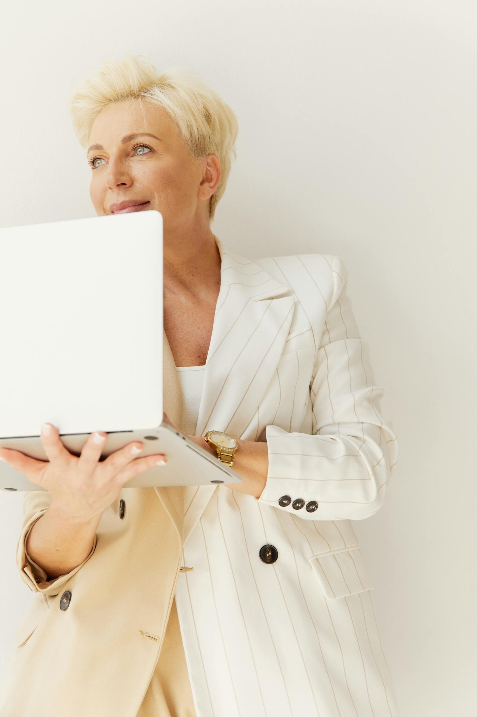 A confident mature businesswoman smiling while using a laptop indoors, representing empowerment and remote work.